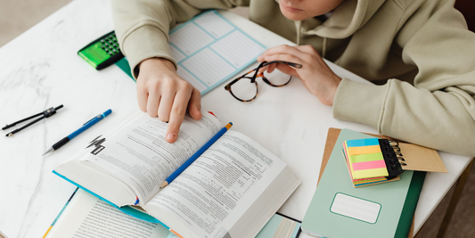 Student studying homeschool curriculum with open textbook, notebook, and school supplies at a desk