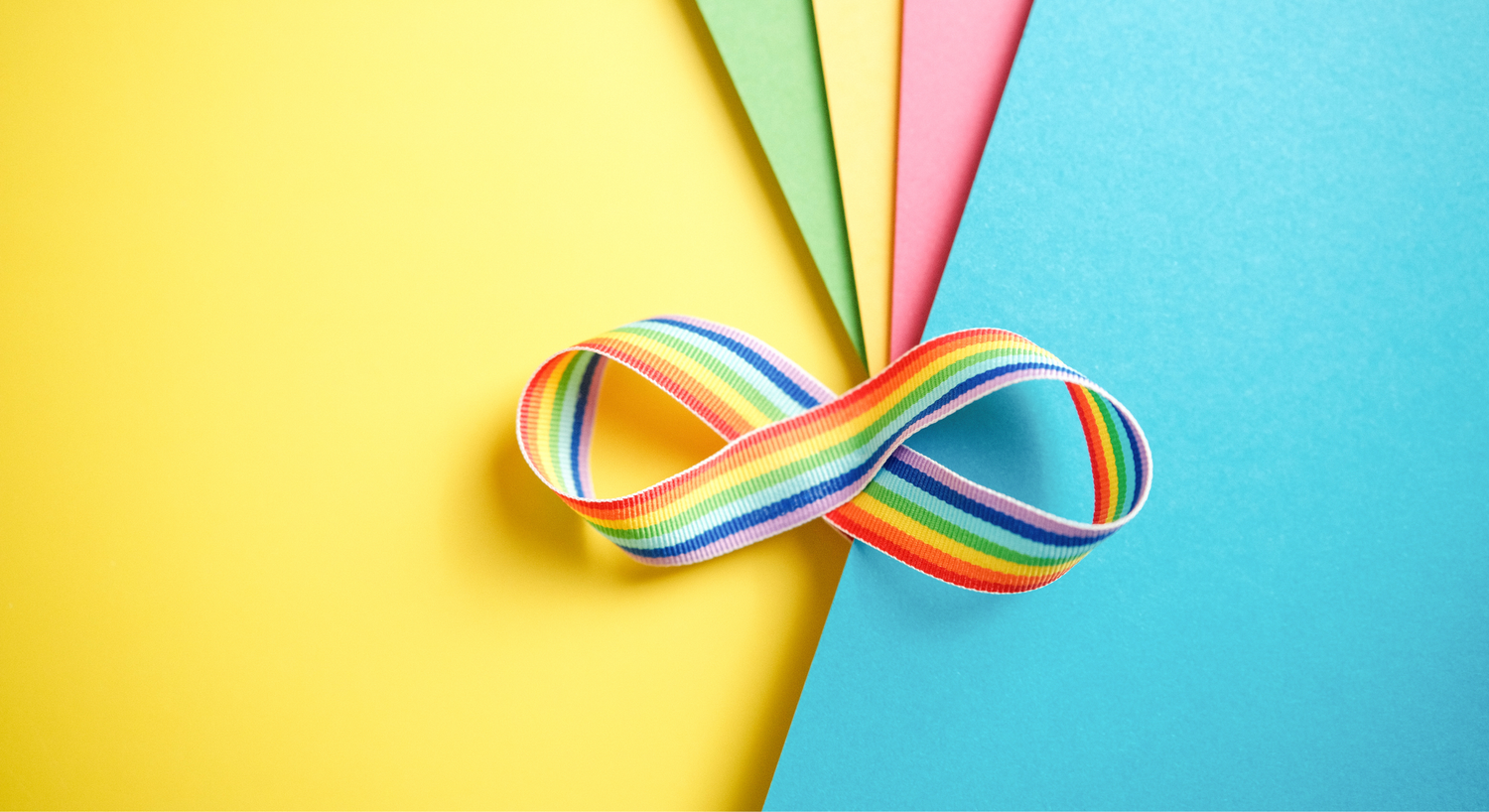 A rainbow infinity-shaped ribbon representing the neurodiversity and inclusion on a stack of colorful construction paper. 